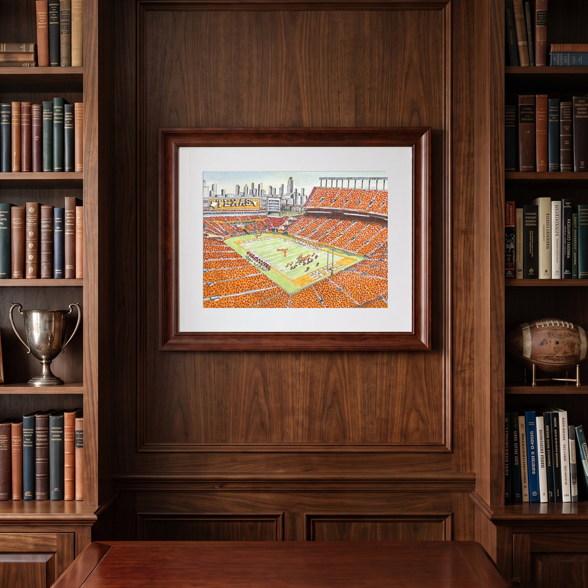 Pen and ink watercolor print of Darrell K Royal-Texas Memorial Stadium framed on a dark library wall.